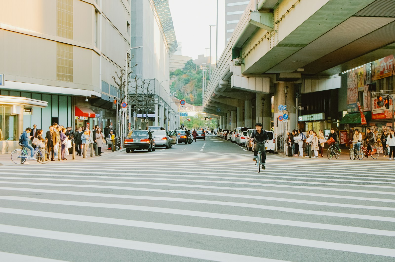 People crossing a busy street with cars and buildings.